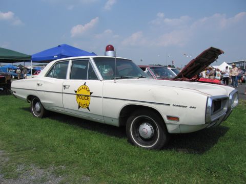 2001 Ford Crown Victoria - This vintage police car is parked on grass with tents and other vehicles in the background under a partly cloudy sky.