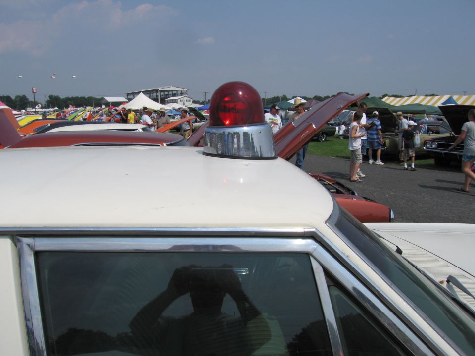 White police car roof with a red light, chrome trim, and reflection of a person holding a camera