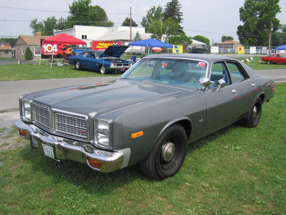 Gray sedan parked on grass, front quarter view. Chrome bumper, square headlights, and a prominent grille are visible
