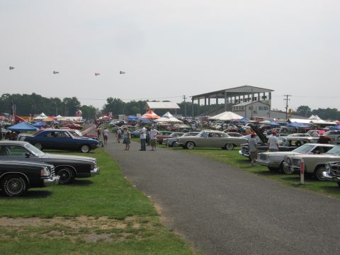 2001 Ford Crown Victoria - A large gathering of classic cars is on display at an outdoor event with tents and spectators.