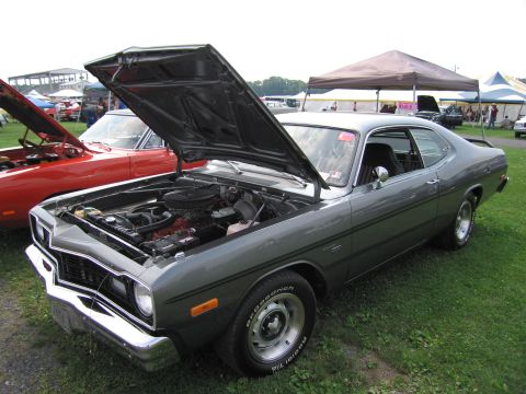 2001 Ford Crown Victoria - A gray 1974 Dodge Dart coupe is displayed with its hood open, revealing the engine compartment, next to a red car.