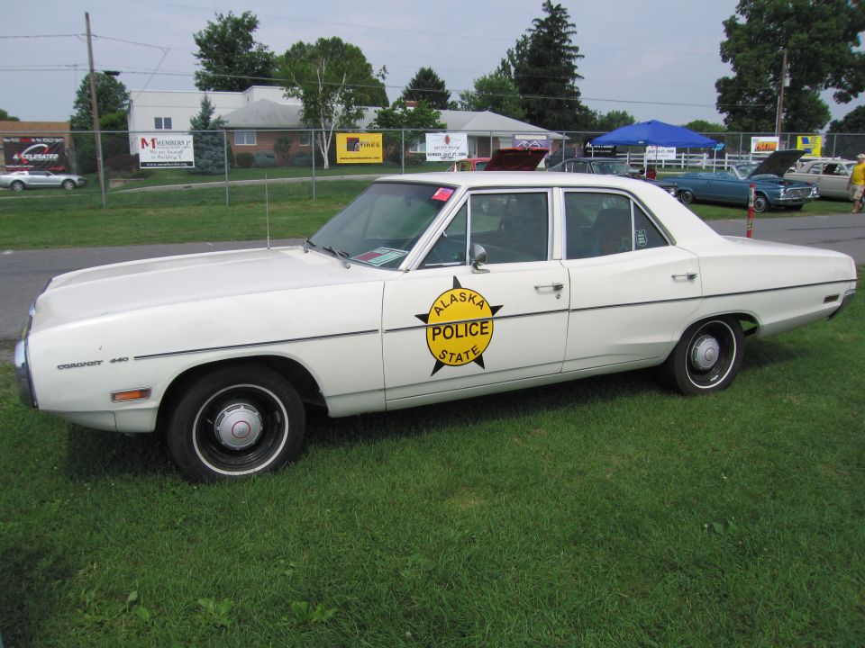 White police car with 'Alaska Police State' badge on the door