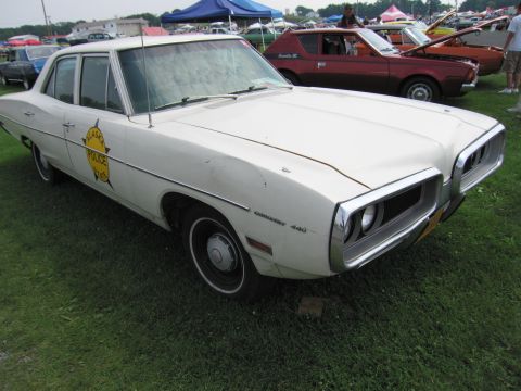 2001 Ford Crown Victoria - A white 1970 Dodge Coronet 440 police car is parked on grass with other vehicles in the background.