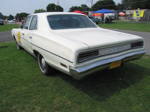 2001 Ford Crown Victoria - White 1970 Dodge sedan, possibly a former police vehicle, parked on grass at an outdoor event.