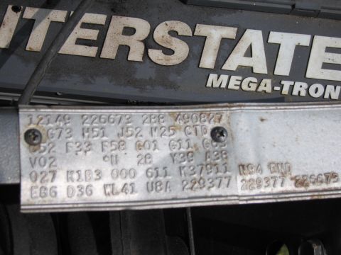 2001 Ford Crown Victoria - Stamped metal vehicle data plate listing VIN, body, and option codes mounted near an Interstate battery.