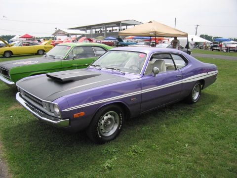 2001 Ford Crown Victoria - A purple Dodge Dart with a black hood scoop and white side stripe is parked on a grassy field next to other cars.