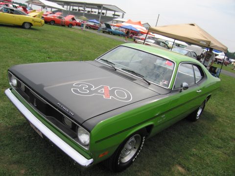 2001 Ford Crown Victoria - A green Plymouth Duster with a black hood displaying a '340' decal is seen at an outdoor car show.