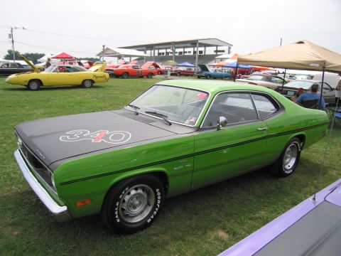 2001 Ford Crown Victoria - A green Plymouth Duster with a '340' decal on its hood is parked on grass at an outdoor event with other cars and tents.