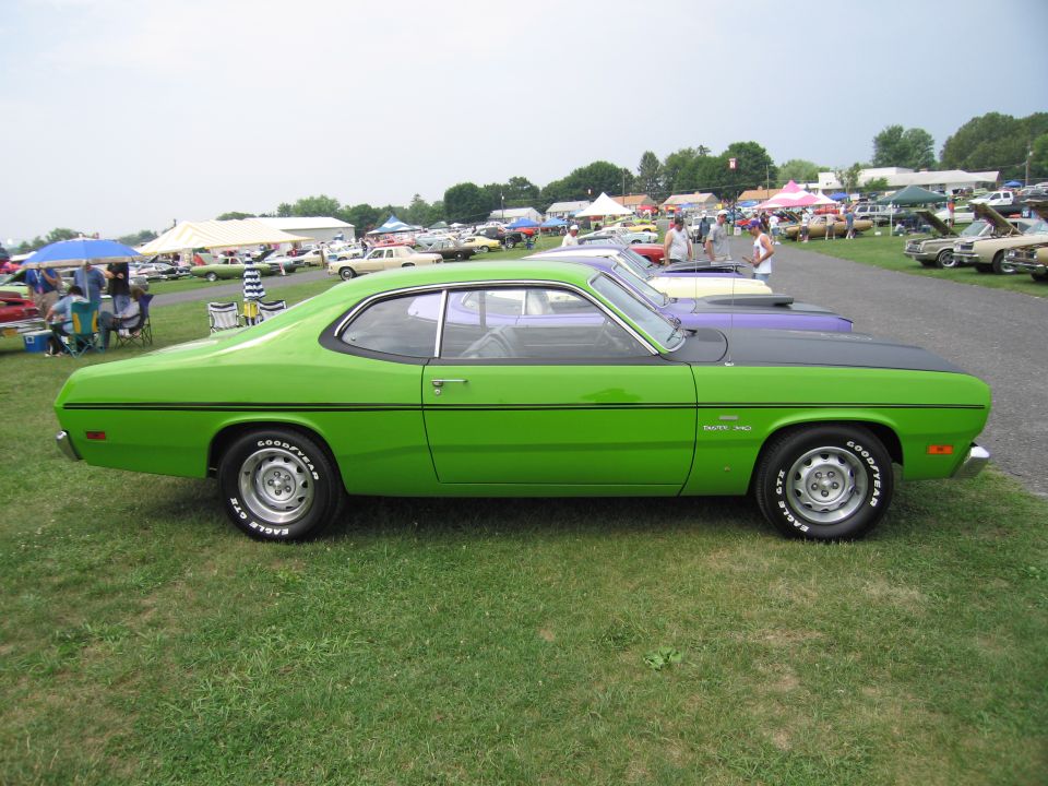 Green muscle car with black hood and racing stripes parked on grass at an outdoor car show