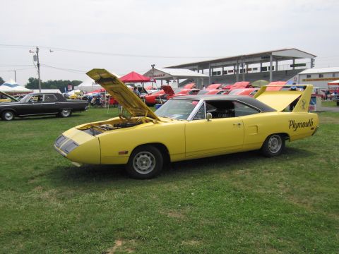 2001 Ford Crown Victoria - A yellow 1970 Plymouth Superbird is displayed with its hood and trunk open at an outdoor car show.