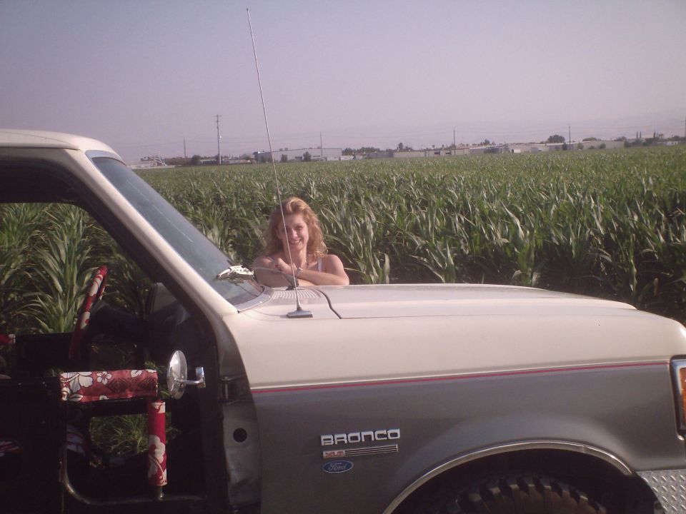 Woman leaning on a white and gray Ford Bronco in front of a cornfield.
