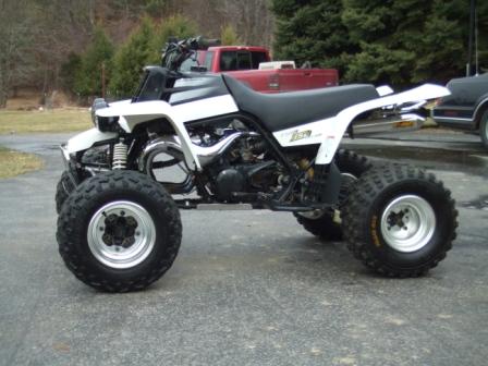 1996 Ford Bronco - Side view of a white and black Yamaha Banshee sport quad parked on a wet asphalt driveway, showing the twin-cylinder two-stroke engine, chr…