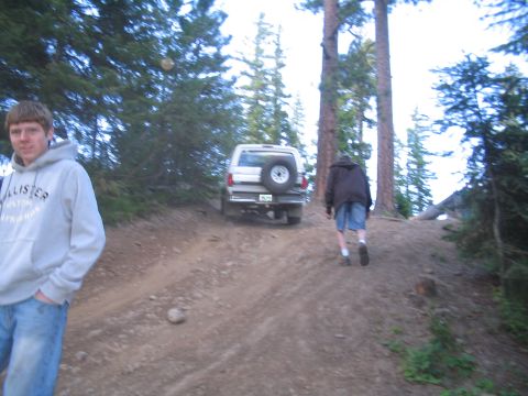 1989 Ford Bronco - A white SUV navigates a steep, wooded trail with a spare tire on its rear.