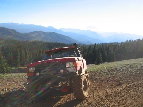 1989 Ford Bronco - A modified red SUV navigates a mountain trail under a clear blue sky.