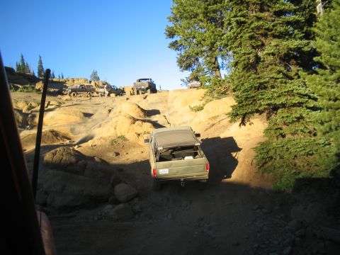 1989 Ford Bronco - Multiple off-road vehicles navigate a challenging dirt trail in a wooded, rocky area.