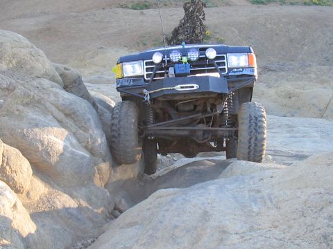 1989 Ford Bronco - An off-road SUV with large tires and auxiliary lights tackles a challenging rocky path.