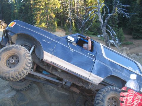 1989 Ford Bronco - This modified SUV is navigating a steep, rocky incline on a dirt trail, with a second vehicle visible in the distance.