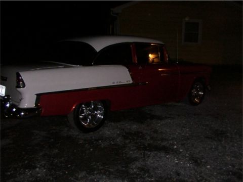 1998 Ford Taurus - A two-tone red and white 1955 Chevrolet Bel Air is parked outside a building at night.