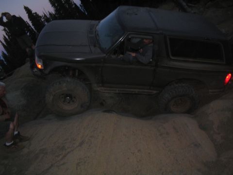 1989 Ford Bronco - SUV with large tires climbs a steep, sandy incline at dusk.