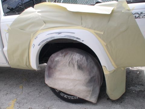 1993 Ford C-350 (Centurion Conversions) - A white pickup truck's fender and wheel are covered in masking materials, indicating preparation for bodywork.