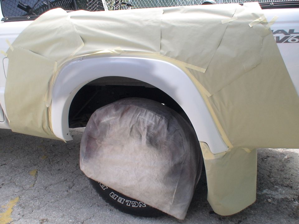 White pickup truck fender and wheel covered in masking tape, with "DUAL V6" visible