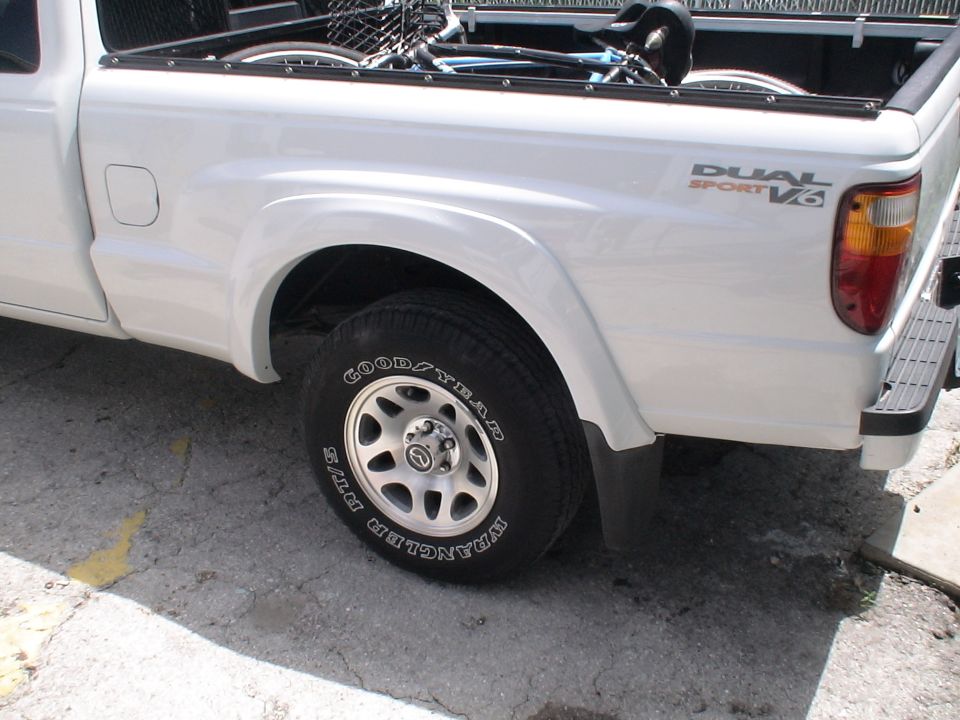 White pickup truck rear fender, wheel, and bed with 'DUAL SPORT V6' badging