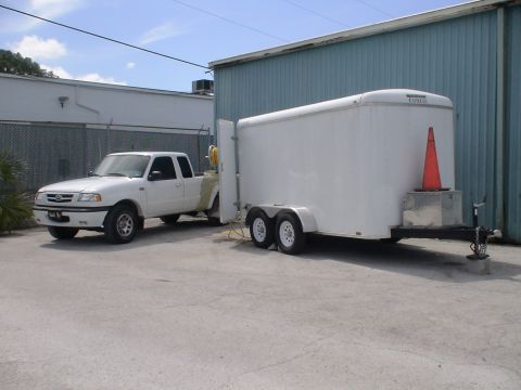 1993 Ford C-350 (Centurion Conversions) - A white Mazda pickup truck is hitched to a white enclosed cargo trailer, parked outdoors.