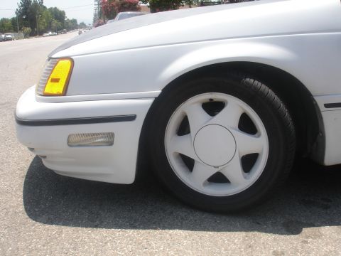 1990 Ford Taurus - Front driver's side corner of a white 1990 Ford Taurus, the wheel and front bumper details.
