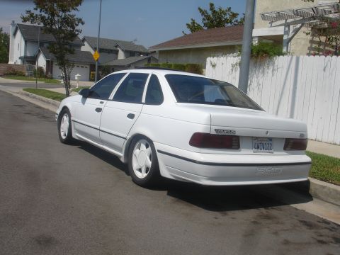 1990 Ford Taurus - Rear view of a white 1990 Ford Taurus sedan parked curbside on a sunny day.
