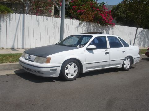 1990 Ford Taurus - A white 1990 Ford Taurus sedan with a gray hood is parked on the street.