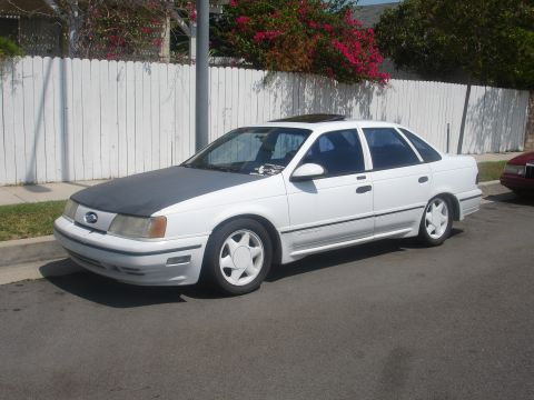 1990 Ford Taurus - A white 1990 Ford Taurus sedan with a dark hood and a sunroof is parked on the street.