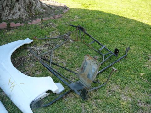 1988 Ford Bronco - Assorted car parts, including a fender and a metal frame, are displayed on a grassy lawn.