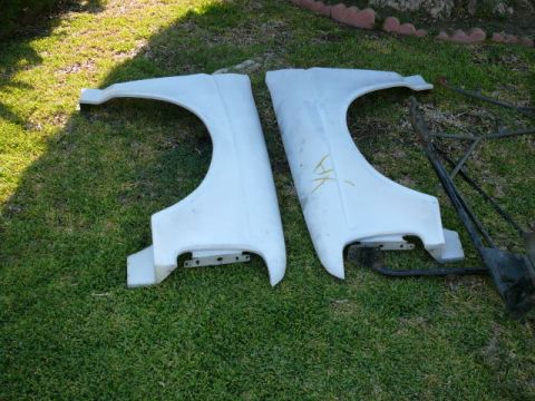 1988 Ford Bronco - Two white fiberglass fenders are shown lying on a grassy surface, with some metal framing visible to the right.
