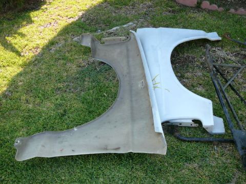 1988 Ford Bronco - Two vehicle fenders, one appearing to be fiberglass and the other metal, lie on a grassy surface.