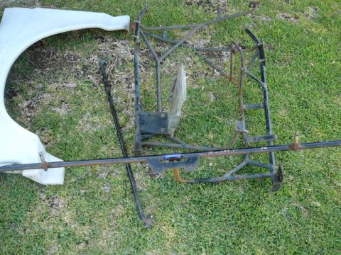 1988 Ford Bronco - A disassembled vehicle frame and a white fender are laid out on the grass, with a Supermotors.net watermark.
