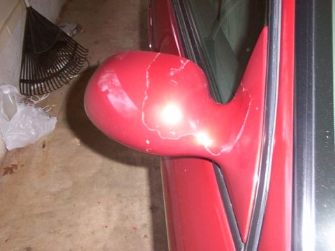 1998 Ford Taurus - A red car side mirror shows signs of wear and peeling paint.
