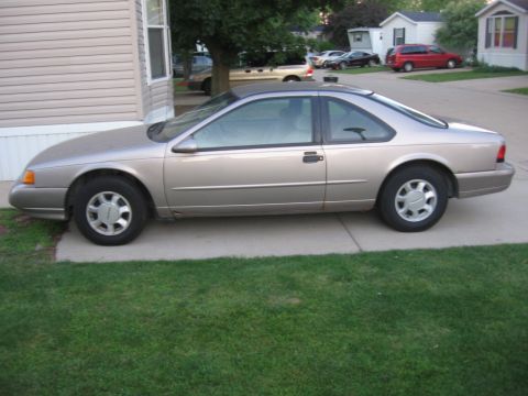 1995 Ford Thunderbird - Side profile of a tan 1995 Ford Thunderbird coupe parked on a concrete driveway.