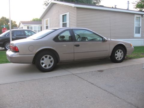 1995 Ford Thunderbird - Side view of a tan Ford Thunderbird parked in front of a beige mobile home.