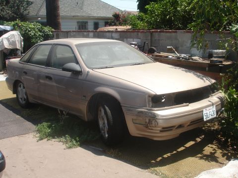 1991 Ford Taurus - This 1991 Ford Taurus sedan shows damage to its front end and appears to be parked in a yard.