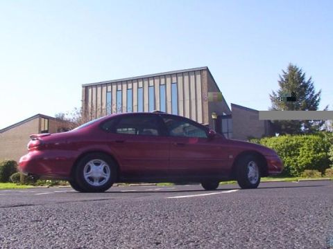 1998 Ford Taurus - A red 1998 Ford Taurus sedan is seen from the side in front of a modern building.