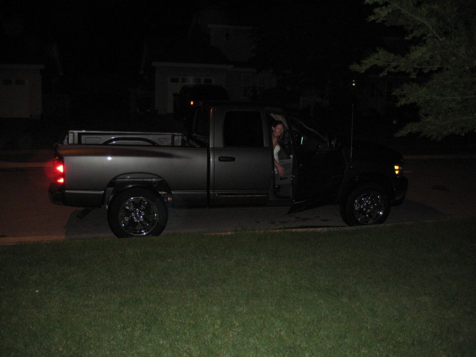 Dark gray Dodge Ram pickup truck with chrome wheels, driver's door open, person inside, brake lights on.