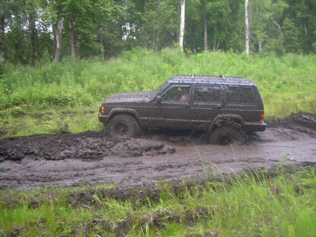 Dark SUV stuck in mud on a wooded trail.
