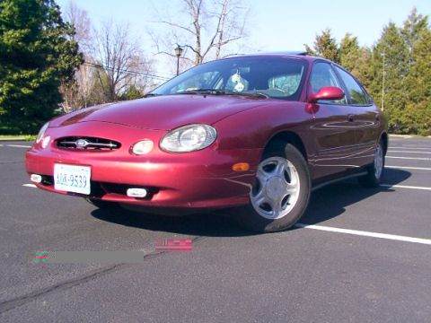 1998 Ford Taurus - A red sedan is parked in a lot on a sunny day. The vehicle appears to be a 1998 Ford Taurus.