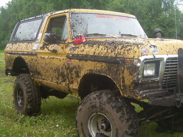 Mud-covered yellow 1978 Ford Bronco with large tires parked in a grassy field.