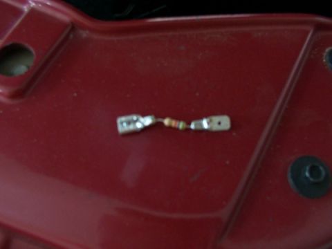 1998 Ford Taurus - A small electrical component with two metal connectors is shown on a red background.