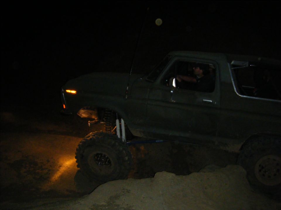 Lifted truck driving over sand at night with driver visible