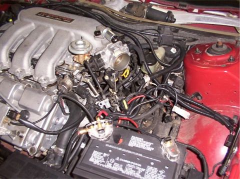 1998 Ford Taurus - Close-up view of engine components, including the manifold and throttle body, with visible wiring and a car battery.