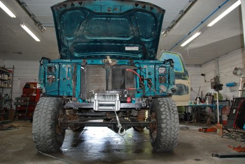 1996 Ford Bronco - Photograph of a lifted teal pickup truck with the hood up undergoing work in a shop, not a document.