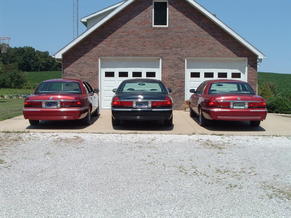 Three sedans parked in front of a brick garage.