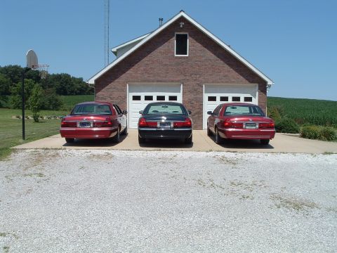 2001 Mercury Grand Marquis - Three sedans are parked in front of a two-car garage on a sunny day.